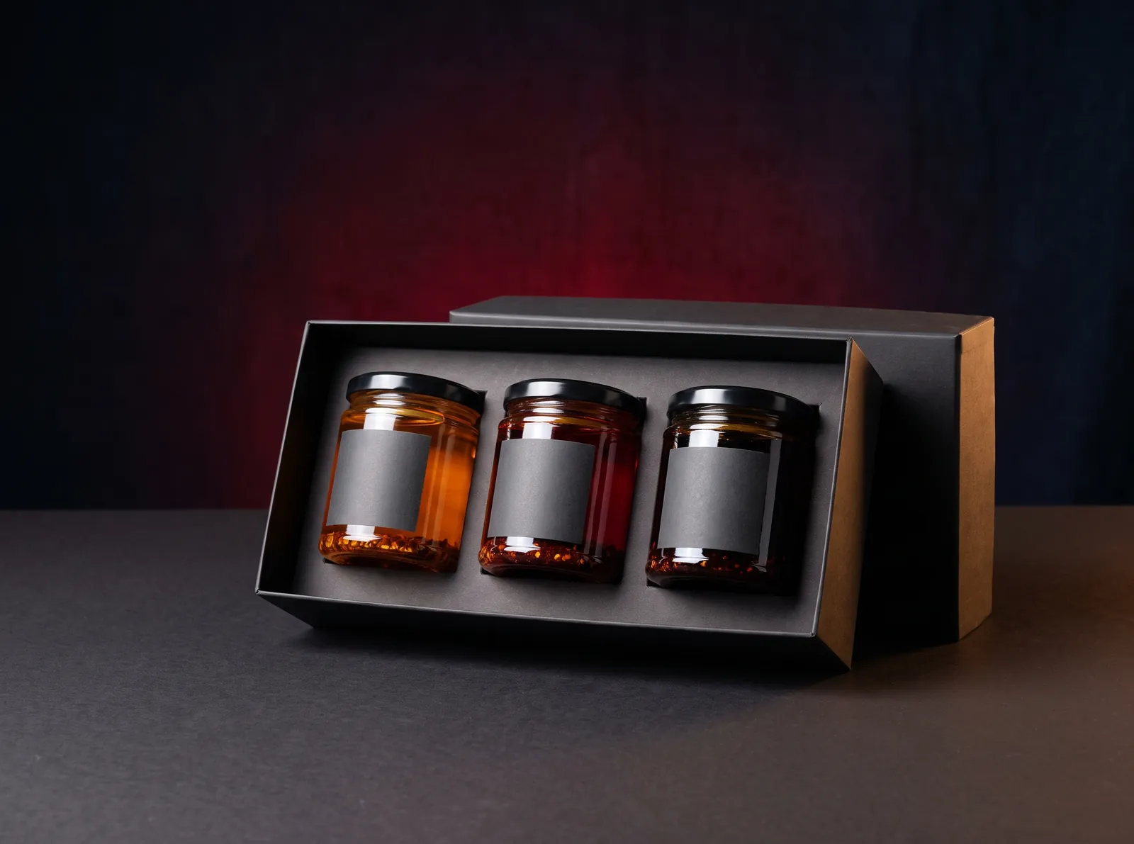 A black gift box holding three jars of chilli oil, from light amber to almost black red.